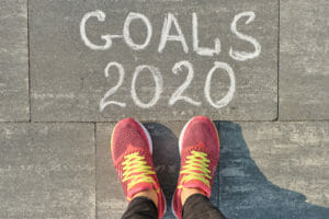 2020 goals, written on gray sidewalk with woman legs in sneakers, top view